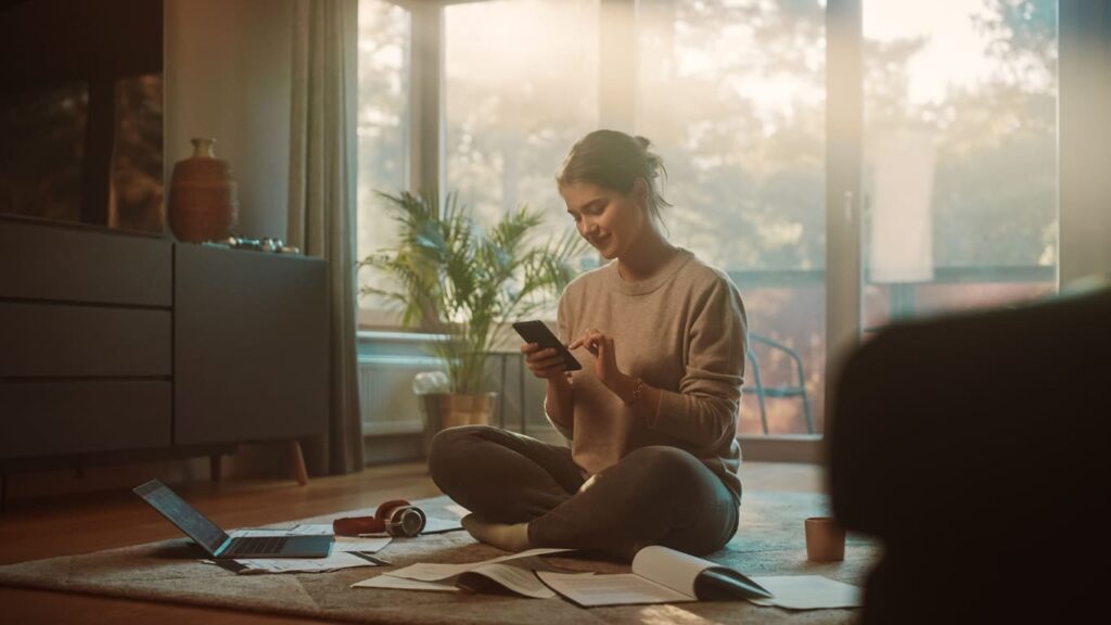 ragazza che studia sul tappeto di casa con cellulare e fogli per terra
